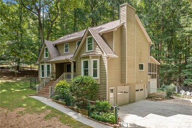 Chalet / cabin featuring roof with shingles, concrete driveway, a garage, a chimney, and view of wooded area