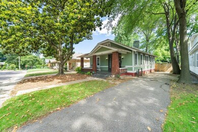 Bungalow-style home with covered porch, a chimney, brick siding, and driveway