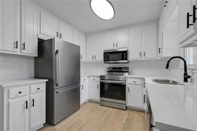 Kitchen featuring appliances with stainless steel finishes, a sink, tasteful backsplash, and light countertops
