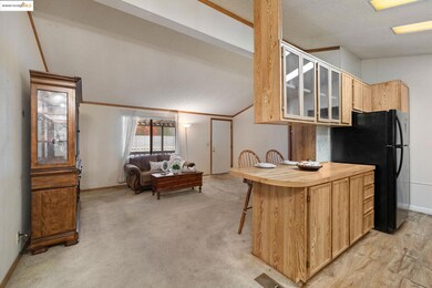 Kitchen featuring a kitchen breakfast bar, vaulted ceiling, glass insert cabinets, light brown cabinets, and freestanding refrigerator