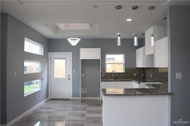 Kitchen featuring white cabinetry, backsplash, kitchen peninsula, dark stone counters, and decorative light fixtures