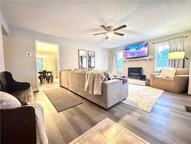 Living area with wood finished floors, ceiling fan, a chandelier, a fireplace with raised hearth, and a textured ceiling