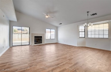 Unfurnished living room with light wood finished floors, a fireplace, a ceiling fan, a chandelier, and vaulted ceiling