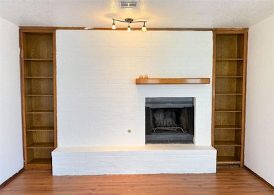 Unfurnished living room with a textured ceiling, a brick fireplace, wood finished floors, and a textured wall