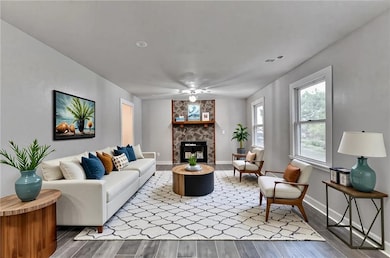 Living room with wood finished floors, a stone fireplace, and ceiling fan