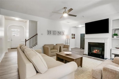 Living room featuring wood finished floors, a fireplace with flush hearth, a ceiling fan, and stairway