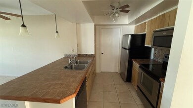 Kitchen with kitchen peninsula, appliances with stainless steel finishes, sink, light tile patterned floors, and pendant lighting