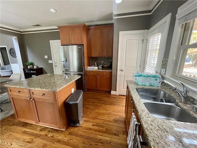 Kitchen with stainless steel refrigerator with ice dispenser, light wood finished floors, ornamental molding, a sink, and brown cabinets