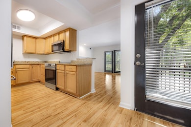 Kitchen with stainless steel appliances, light wood-style flooring, ornamental molding, a tray ceiling, and light brown cabinetry