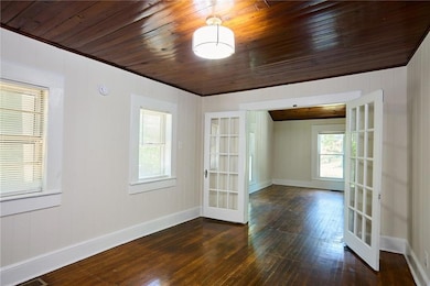 Unfurnished room featuring french doors, wood walls, dark wood finished floors, wood ceiling, and crown molding