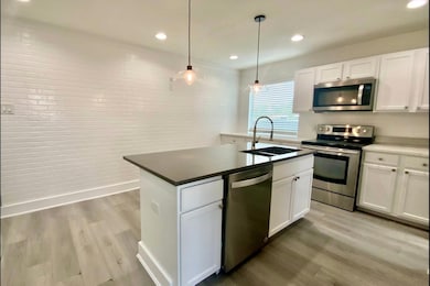 Kitchen with stainless steel appliances, white cabinets, light wood-type flooring, a kitchen island with sink, and recessed lighting