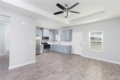 Kitchen with stainless steel appliances, a raised ceiling, a sink, light countertops, and ceiling fan