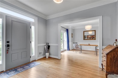 Entrance foyer featuring crown molding, light wood-style flooring, a wainscoted wall, and a decorative wall