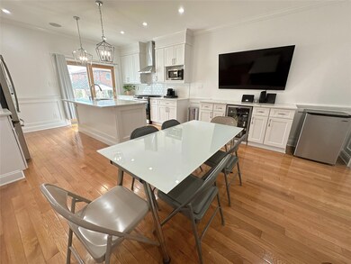 Kitchen featuring light wood finished floors, appliances with stainless steel finishes, a sink, beverage cooler, and wall chimney range hood