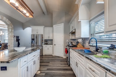 Kitchen with dark stone countertops, arched walkways, white cabinets, dark wood-style flooring, and stainless steel appliances