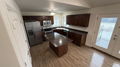 Kitchen featuring light wood finished floors, dark countertops, appliances with stainless steel finishes, a center island, and pendant lighting