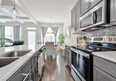 Kitchen featuring stainless steel appliances, a sink, gray cabinetry, beam ceiling, and a chandelier