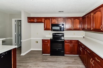 Kitchen featuring black appliances, light countertops, a textured ceiling, light wood-style flooring, and dark brown cabinets