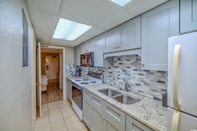 Kitchen featuring white appliances, a sink, backsplash, light tile patterned flooring, and a drop ceiling