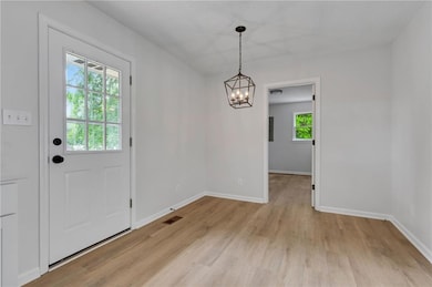 Unfurnished dining area featuring a chandelier, light wood-style flooring, and baseboards