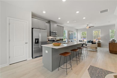 Kitchen with gray cabinetry, appliances with stainless steel finishes, a kitchen island with sink, recessed lighting, and a kitchen breakfast bar