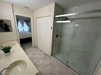 Bathroom featuring a sink, a marble finish shower, visible vents, and a textured ceiling