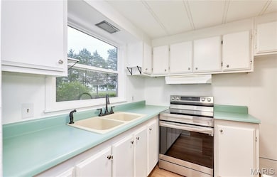 Kitchen with stainless steel range with electric cooktop, white cabinets, light countertops, under cabinet range hood, and light wood-type flooring