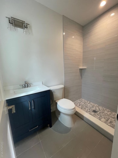 Bathroom featuring vanity, tile patterned flooring, a tile shower, and recessed lighting