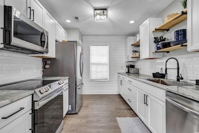 Kitchen featuring tasteful backsplash, appliances with stainless steel finishes, open shelves, a textured ceiling, and wood finished floors