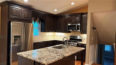 Kitchen with dark brown cabinetry, stainless steel appliances, vaulted ceiling, recessed lighting, and backsplash