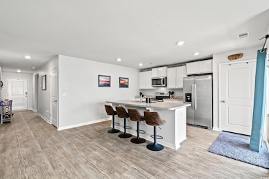 Kitchen featuring appliances with stainless steel finishes, light wood finished floors, white cabinetry, a center island with sink, and recessed lighting