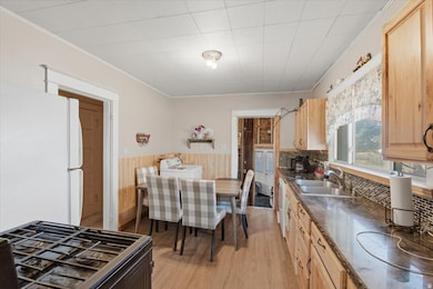 Kitchen featuring black gas stove, light wood-style flooring, ornamental molding, wainscoting, and freestanding refrigerator