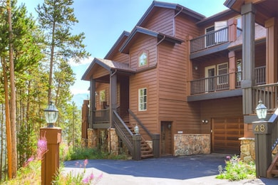Chalet / cabin featuring stairway, stone siding, a balcony, an attached garage, and asphalt driveway