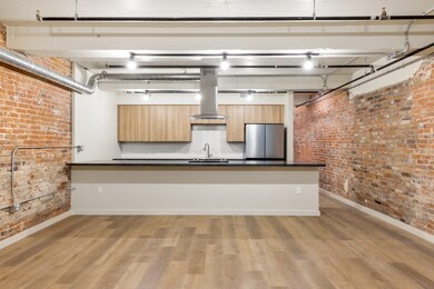 Kitchen featuring sink, island range hood, light wood-type flooring, stainless steel refrigerator, and brick wall