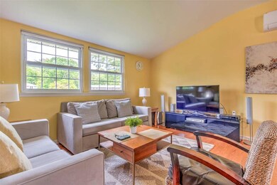 Living room with wood finished floors, a wall mounted air conditioner, and vaulted ceiling