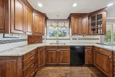 Kitchen with light stone counters, dishwasher, healthy amount of natural light, glass insert cabinets, and recessed lighting