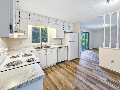 Kitchen with white appliances, under cabinet range hood, wood finished floors, white cabinets, and a textured ceiling