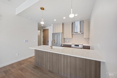 Kitchen with modern cabinets, tasteful backsplash, light stone counters, wall chimney exhaust hood, and dark wood-style floors
