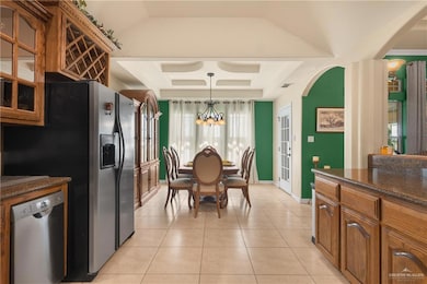 Kitchen featuring brown cabinets, dark stone counters, decorative light fixtures, and stainless steel dishwasher