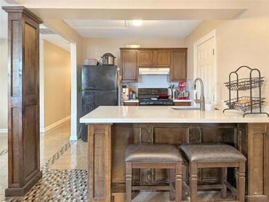 Kitchen featuring under cabinet range hood, baseboards, backsplash, a sink, and black appliances