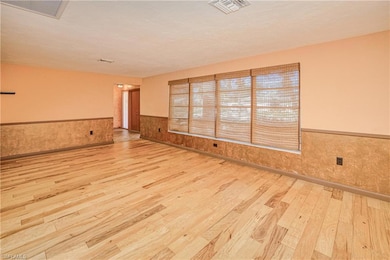 Unfurnished room with a wainscoted wall, light wood-type flooring, and a textured ceiling
