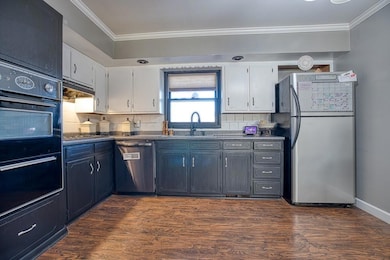 Kitchen featuring stainless steel appliances, dark countertops, ornamental molding, white cabinets, and under cabinet range hood