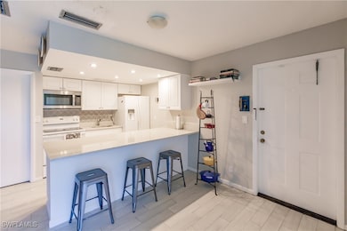 Kitchen featuring white appliances, sink, kitchen peninsula, a kitchen bar, and white cabinetry