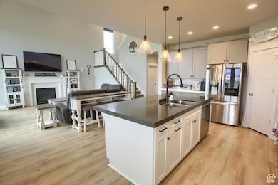 Kitchen with a sink, appliances with stainless steel finishes, dark countertops, a kitchen island with sink, and light wood-style floors