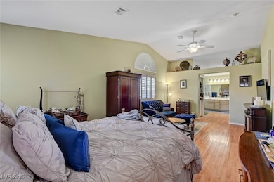 Bedroom featuring light wood-style floors, lofted ceiling, ensuite bath, and ceiling fan