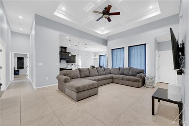 Living area featuring coffered ceiling, recessed lighting, ceiling fan with notable chandelier, baseboards, and a high ceiling