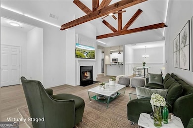Living room featuring beamed ceiling, a fireplace with flush hearth, wood finished floors, a chandelier, and ceiling fan