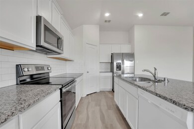 Kitchen with light stone countertops, white cabinetry, sink, appliances with stainless steel finishes, and light wood-type flooring