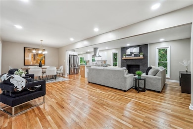 Living area with light wood-style flooring, a fireplace, a chandelier, baseboards, and recessed lighting