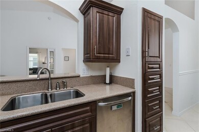Kitchen with stainless steel dishwasher, arched walkways, light tile patterned flooring, and brown cabinetry